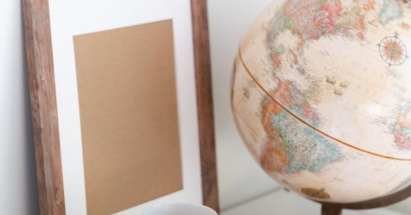 Retro Home - Vintage globe near blank frame and cup of tea placed on book in office