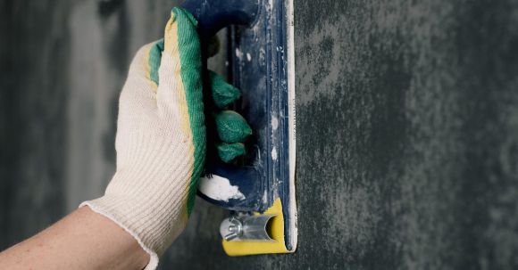 DIY Projects - Crop anonymous male worker in gloves holding scraper and aligning walls in flat