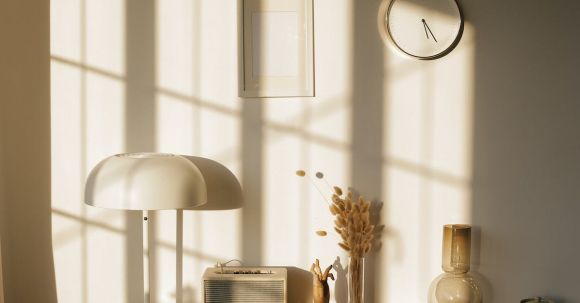 Retro Home - Light room with retro radio and decorative vases with dry plants on desk near wall with clock and window shadow in sunlight