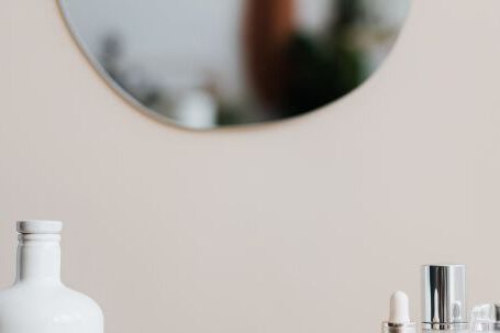 Storage Hacks - Reusable cosmetic containers for cream and shower gel arranged near various skincare products and perfume bottle on white marble shelf against beige wall with mirror in elegant bathroom interior