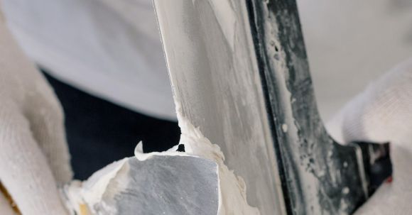 DIY Projects - Crop unrecognizable male in gloves holding putty knives while working at new home