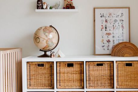 Retro Home - Comfortable bed with toys globe and paintings placed on wooden cabinet with wicker boxes and soft white rug with toy house on floor
