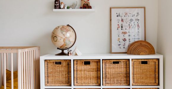 Retro Home - Comfortable bed with toys globe and paintings placed on wooden cabinet with wicker boxes and soft white rug with toy house on floor