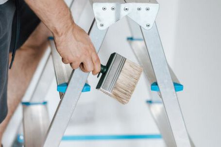 Home Repair - Painter with brush climbing ladder during renovation work