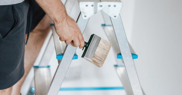 Home Repair - Painter with brush climbing ladder during renovation work