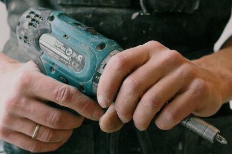 Home Repair - Crop anonymous mechanic in uniform with wireless drill standing in flat during repair works
