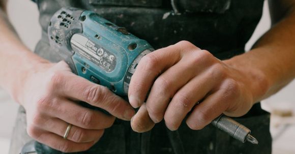 Home Repair - Crop anonymous mechanic in uniform with wireless drill standing in flat during repair works