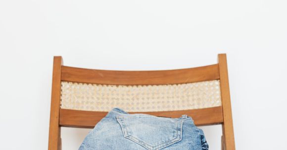 Storage Solutions - Stack of blue jeans of different shades on modern wooden chair against white wall