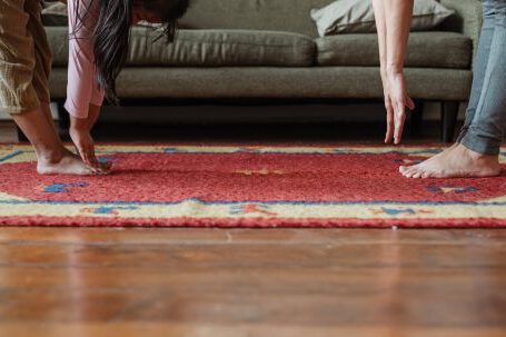 Floor - Side view of young ethnic woman stretching body with adorable girl while standing against each other on floor carpet near cozy sofa in modern living room in morning