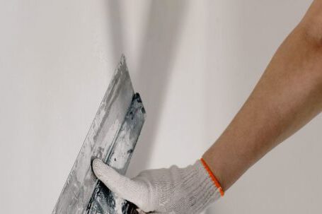 DIY Projects - Crop anonymous male worker in gloves holding putty knife while working at home