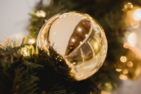 Seasonal Decor - Christmas golden bauble on artificial fir garland full of lights on blurred background